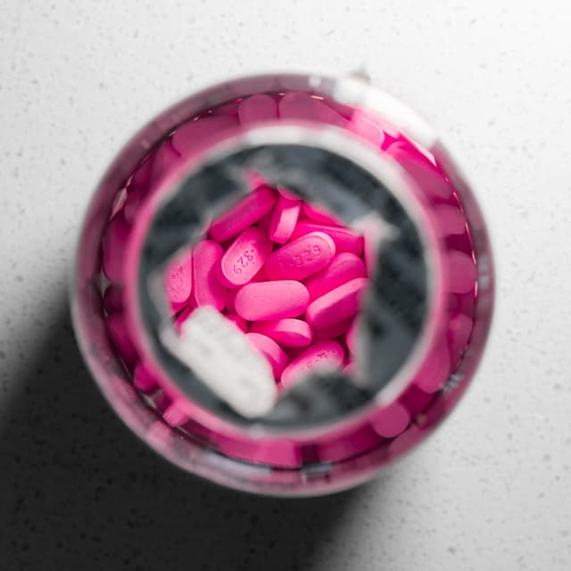A top-down view of a bottle filled with pink pills on a speckled surface