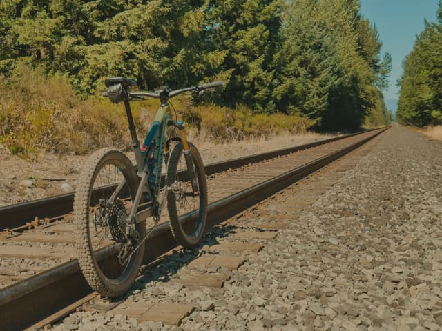 A bicycle is positioned on a railway track surrounded by trees under a clear blue sky