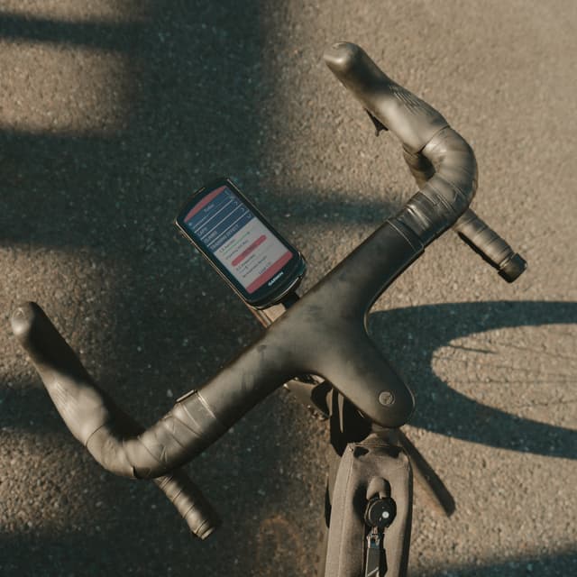 A bicycle handlebar with a smartphone mounted on it, displaying a screen with text, on a sunlit road