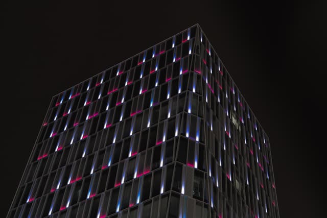 A building with a grid-like facade illuminated by colorful lights against a dark sky
