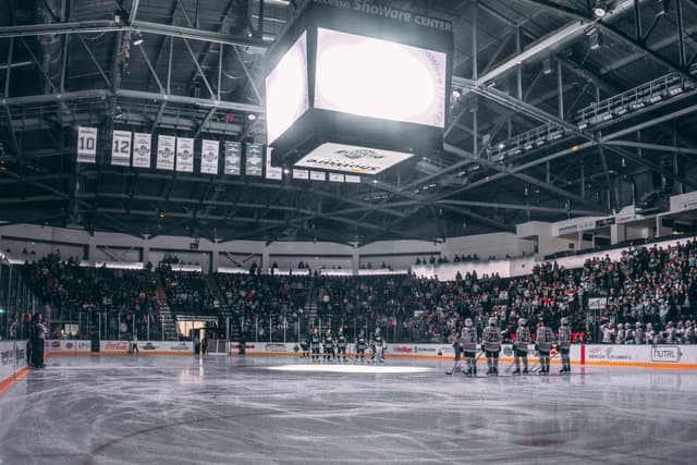 A hockey arena with teams lining up on the ice, surrounded by a large audience