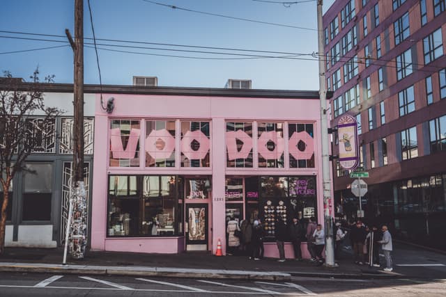 A pink building with large VOODOO letters on the facade, located on a street corner with people gathered outside