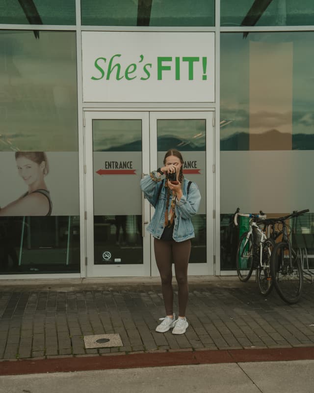 Woman photographing in front of fitness studio with bicycle nearby