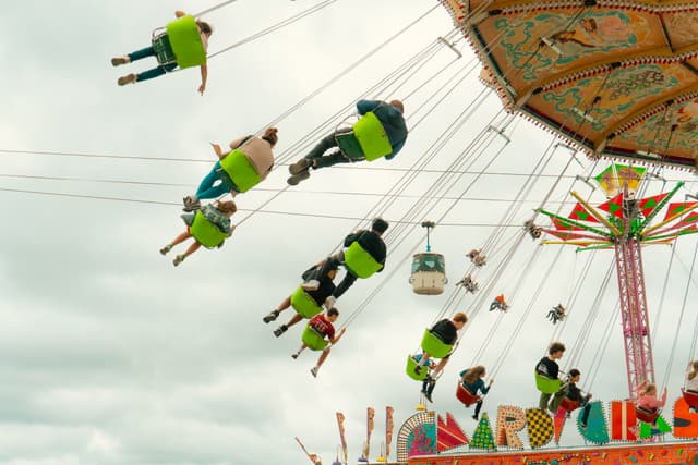 People enjoying a spinning swing ride at an amusement park, with colorful seats suspended by chains and a partly cloudy sky in the background