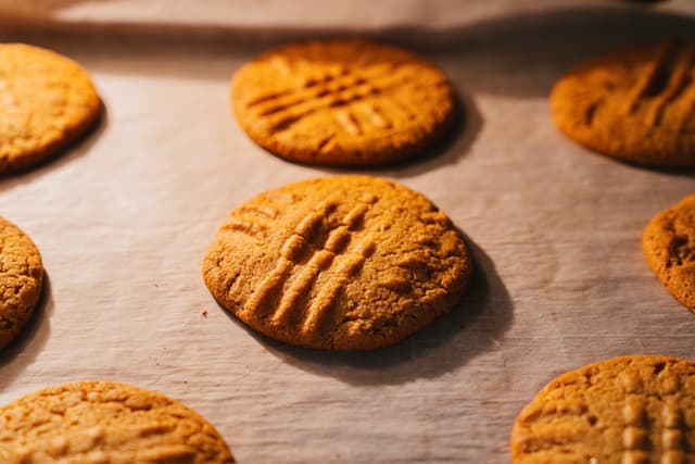 Freshly baked peanut butter cookies with fork marks on parchment paper
