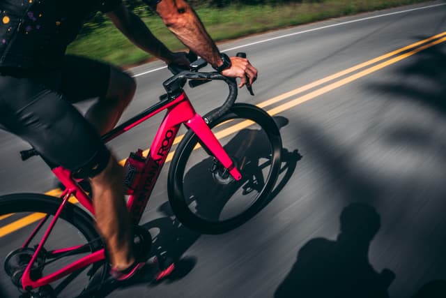 A cyclist riding a red bike on a paved road with yellow lines, casting a shadow on the ground