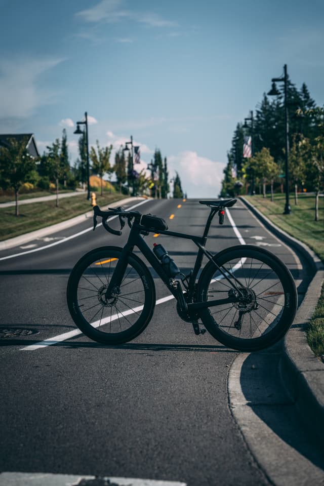 A bicycle is parked on a road with a clear sky and trees lining the street