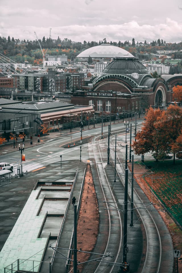 Railway tracks lead to a cityscape with a prominent dome and autumn trees
