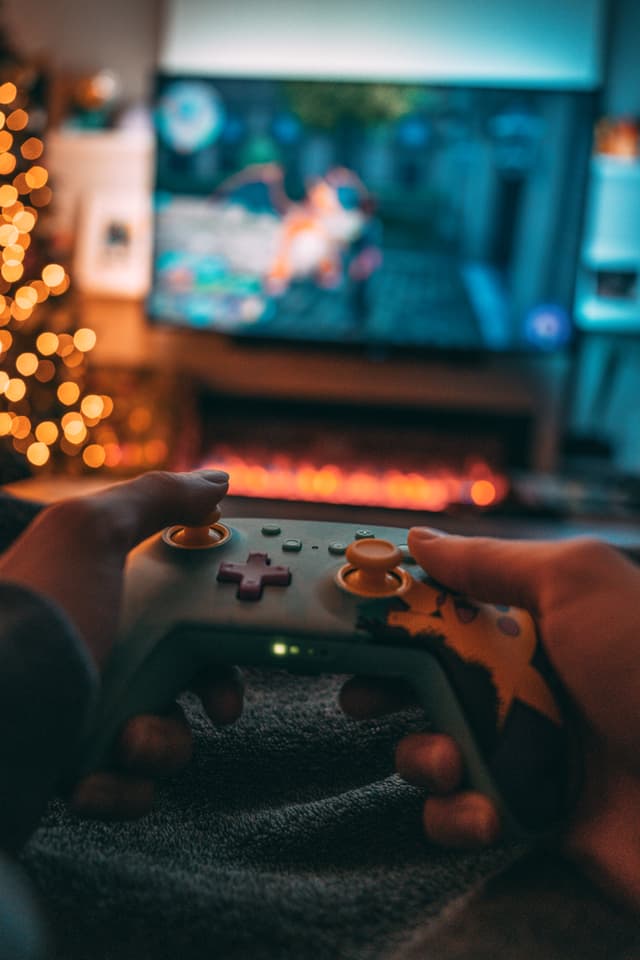 Hands holding a game controller with a video game displayed on a screen in the background