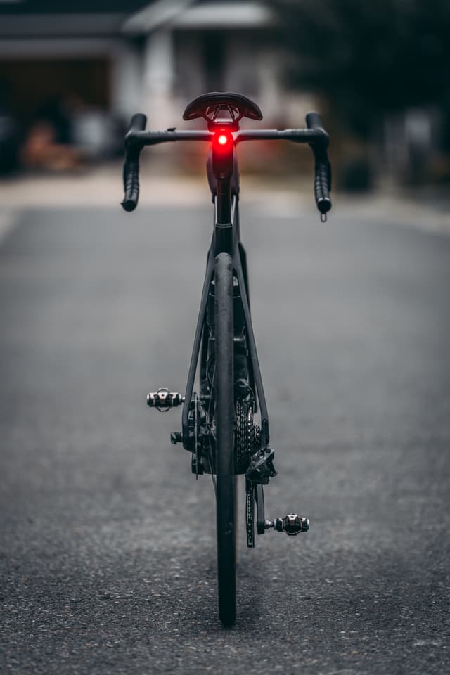 A bicycle with a red rear light is positioned on a road, viewed from behind