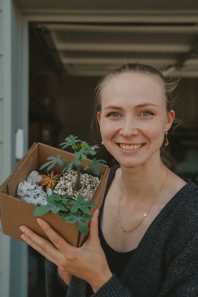 A person smiling and holding a cardboard box containing small plants