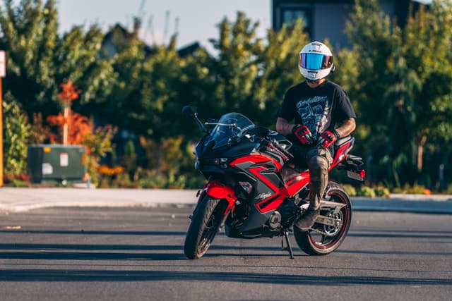 A person wearing a helmet rides a red motorcycle on a paved road, surrounded by greenery