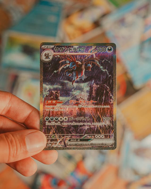 A hand holding a trading card with a dark, stormy design, featuring lightning and a creature, against a blurred background of other cards