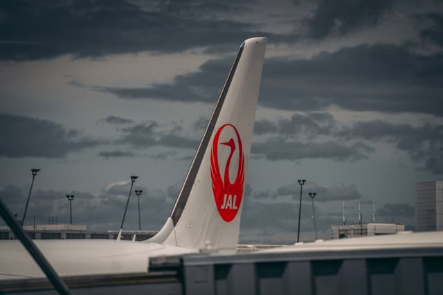 The tail of a Japan Airlines aircraft with a red crane logo against a cloudy sky
