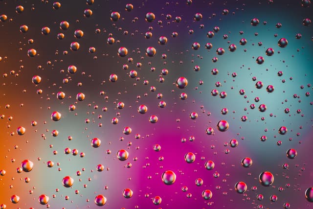 Water droplets on a glass surface with a colorful, blurred background featuring shades of blue, pink, and orange