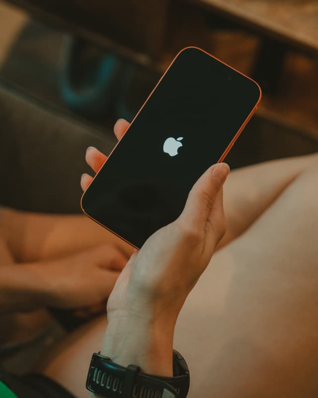 A hand holding a black smartphone with the Apple logo on the screen, alongside a wristwatch on the person's arm