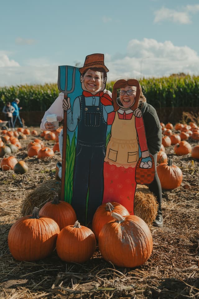 People posing with painted farmer cutouts in a pumpkin patch