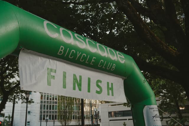 A green inflatable archway with Cascade Bicycle Club and FINISH written on it, set against a backdrop of trees and buildings