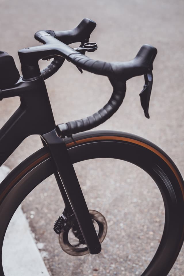 A close-up of a bicycle's front wheel and handlebars, featuring a sleek, modern design with black components and a disc brake