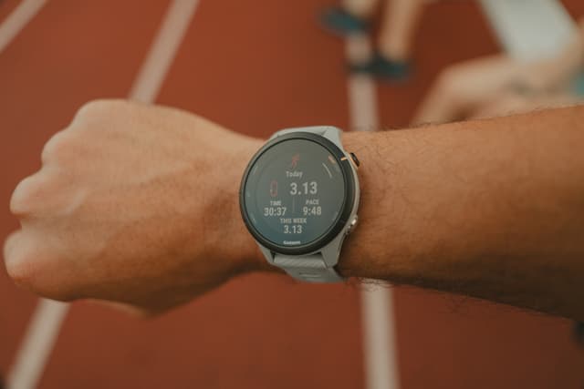 A person wearing a smartwatch on their wrist, displaying running statistics, with a blurred running track in the background