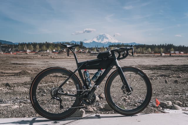 A bicycle is parked on a concrete surface with a mountainous landscape in the background under a clear blue sky