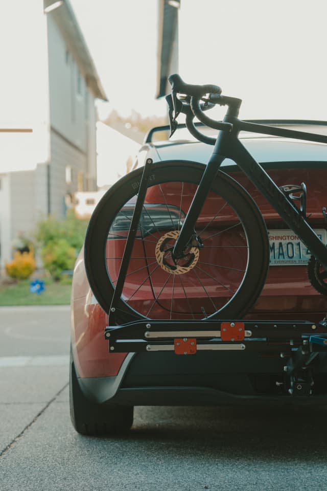 A red car with a bicycle mounted on a rear bike rack, parked in a residential driveway
