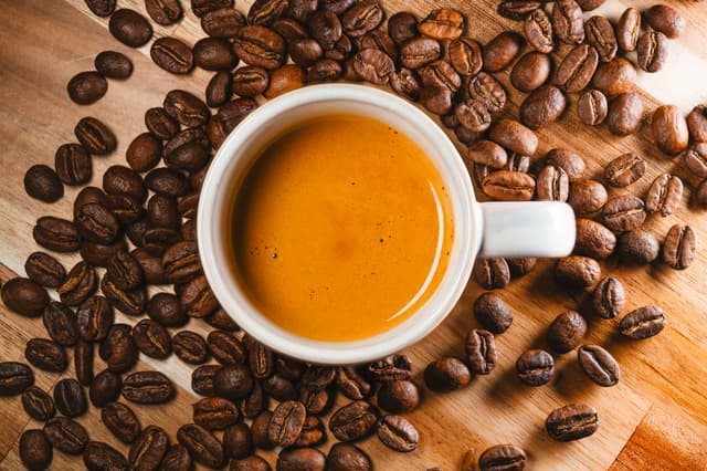 A cup of espresso surrounded by coffee beans on a wooden surface