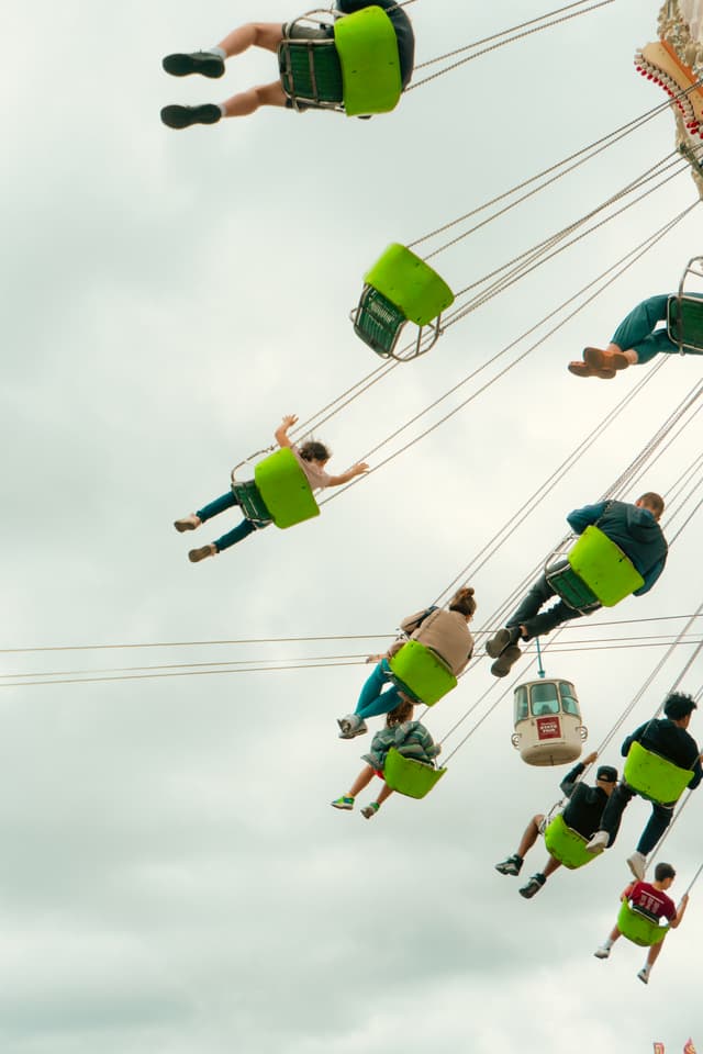 People riding on a spinning swing ride, with seats suspended in the air against a cloudy sky