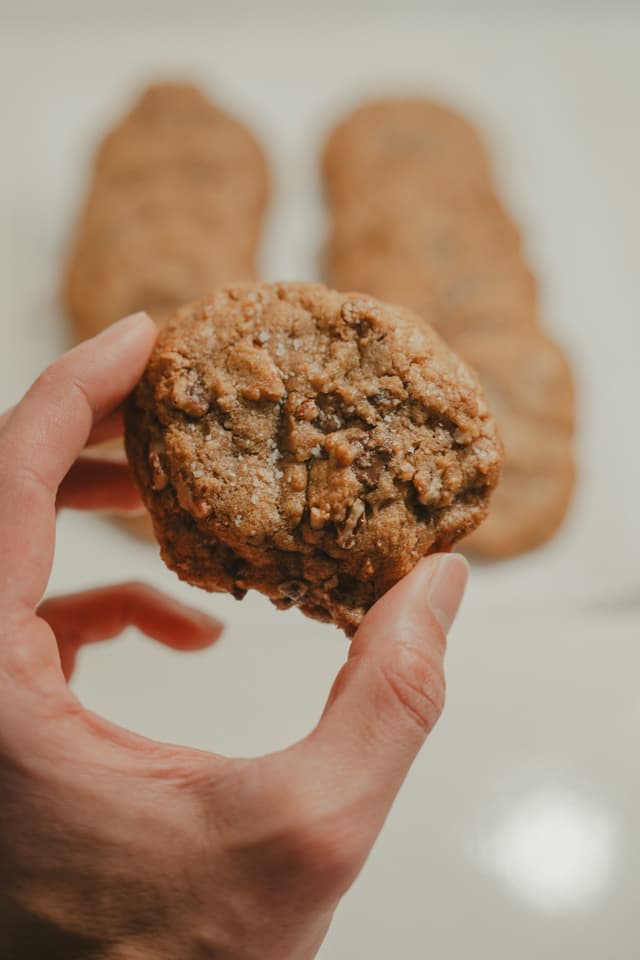 A hand holding a freshly baked cookie with more cookies in the background