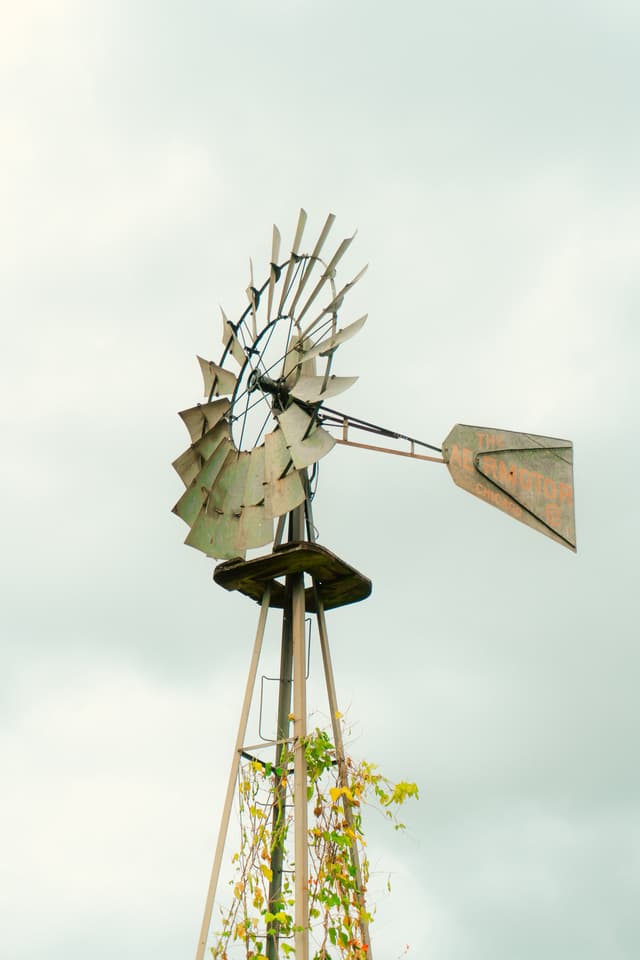 An old-fashioned metal windmill with a partly rusted appearance against a cloudy sky