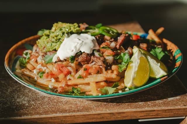 A plate of loaded fries topped with guacamole, sour cream, diced tomatoes, jalapeños, and lime wedges