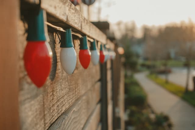 Colorful holiday lights on a wooden fence with a blurred background of a suburban neighborhood