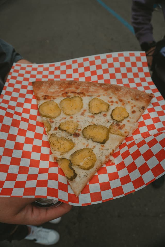A slice of pizza topped with pickles is placed on a red and white checkered paper