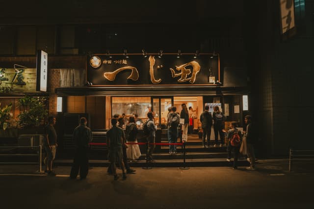 A group of people standing outside a restaurant at night, with a large illuminated sign above the entrance