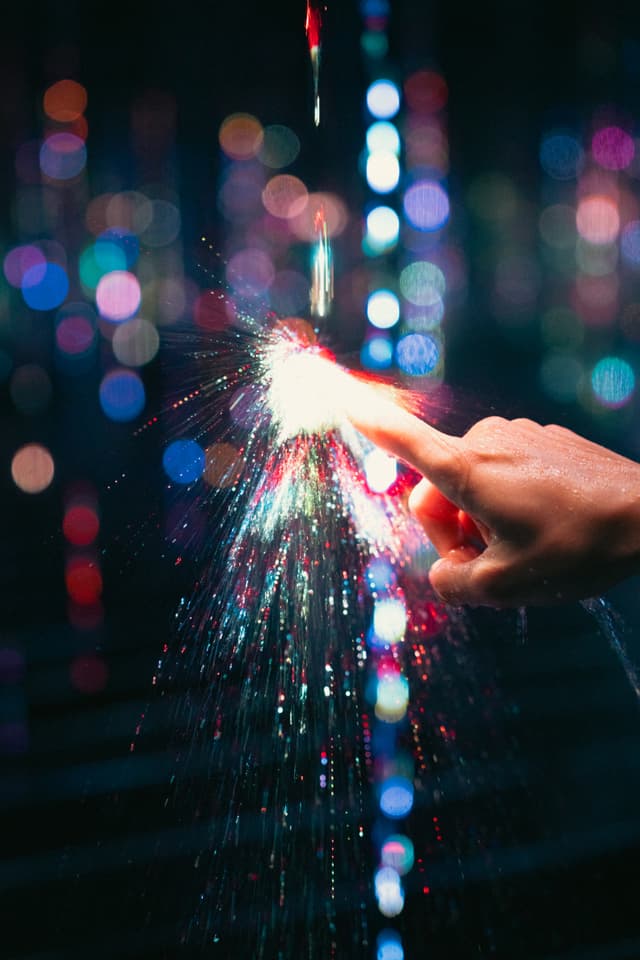A hand touching a stream of light with colorful bokeh effects in the background