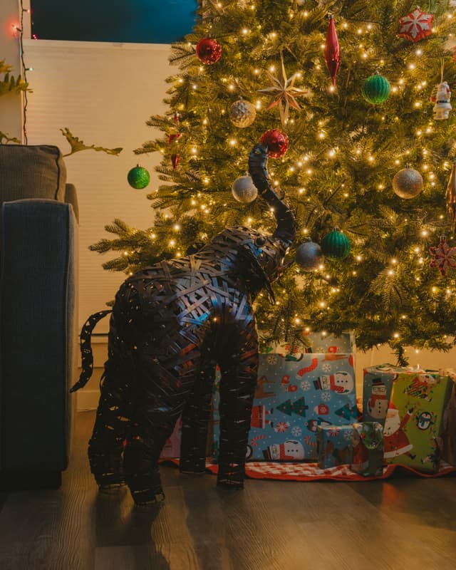 A decorative elephant statue stands beside a lit Christmas tree and presents