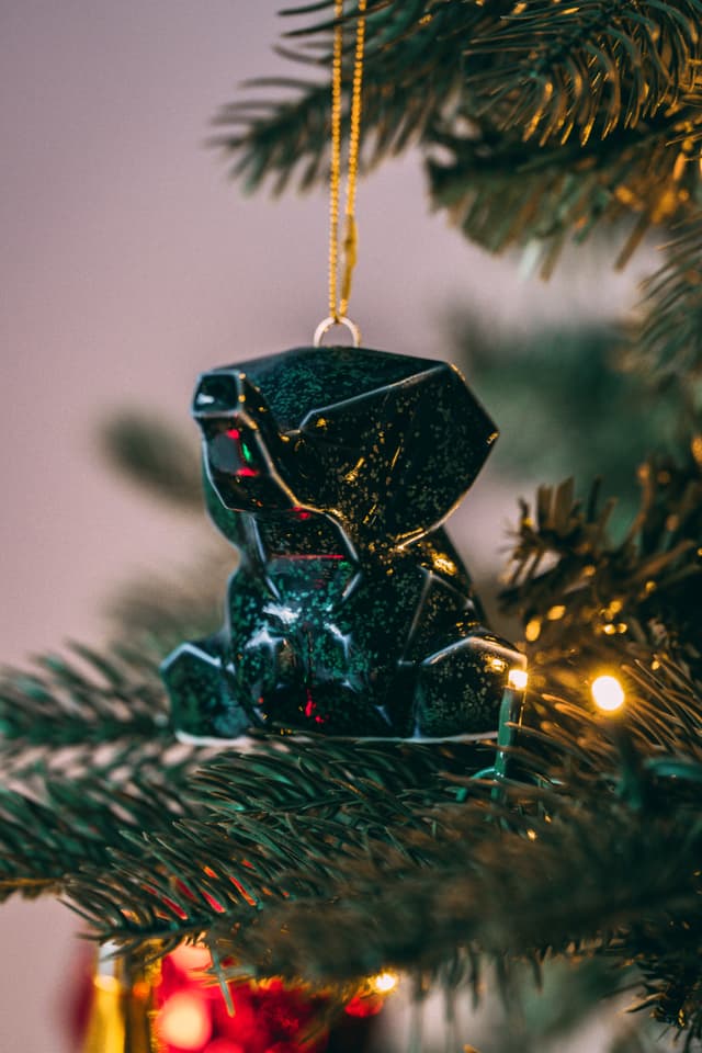 Black geometric ornament hanging on a Christmas tree branch with lights and blurred background