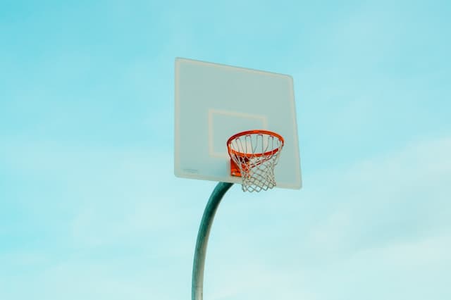 Outdoor basketball hoop with white backboard and net against a clear blue sky