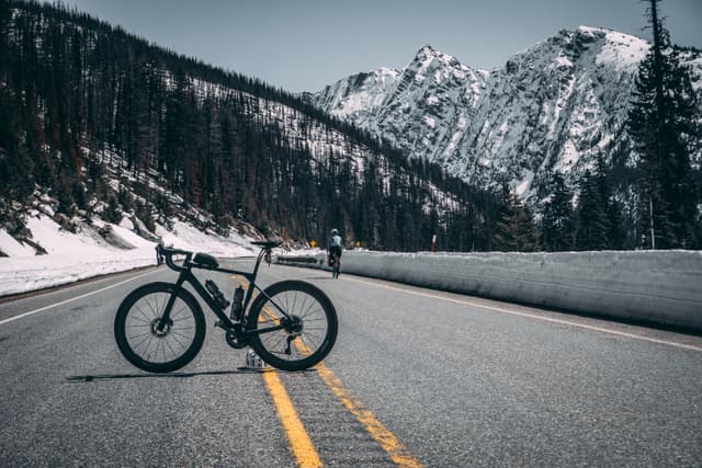 A canyon endurace is parked on a mountain road with snow-covered peaks and pine trees in the background