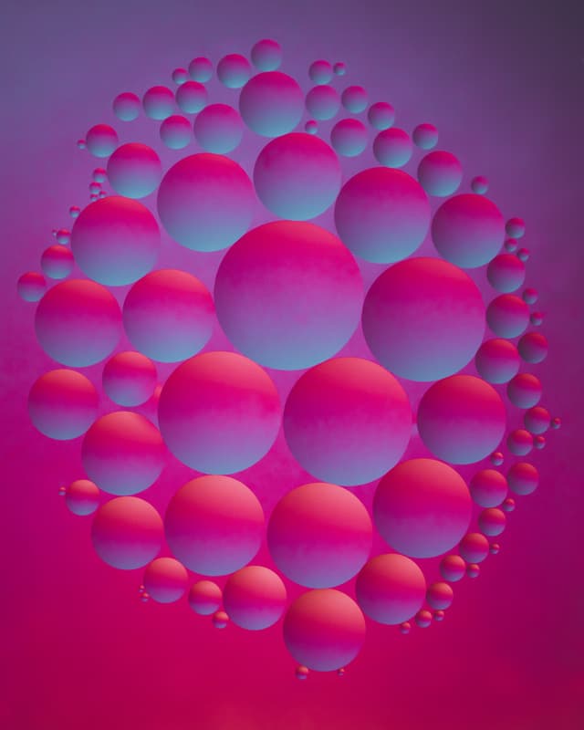 Multiple oil spheres in a gradient of blue and pink hues, arranged in a 3D cluster against a vibrant magenta and purple background