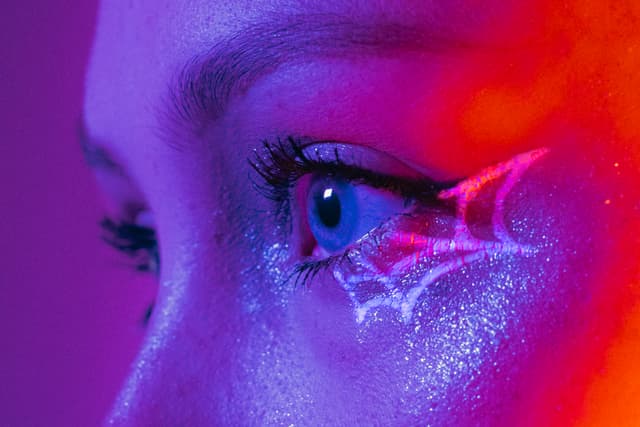 Close-up of a neon-lit eye with artistic makeup and glowing eyelashes