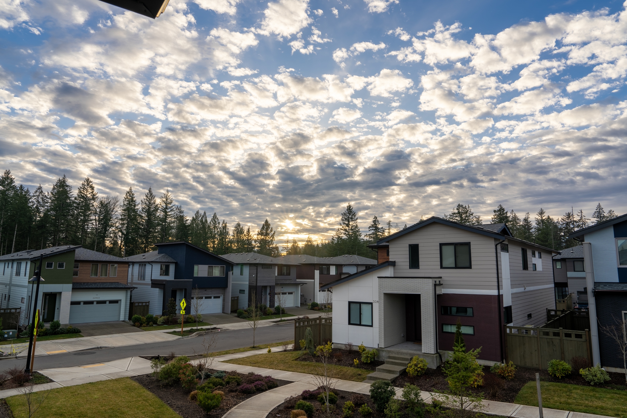 A suburban neighborhood with modern houses under a sky filled with scattered clouds, surrounded by trees
